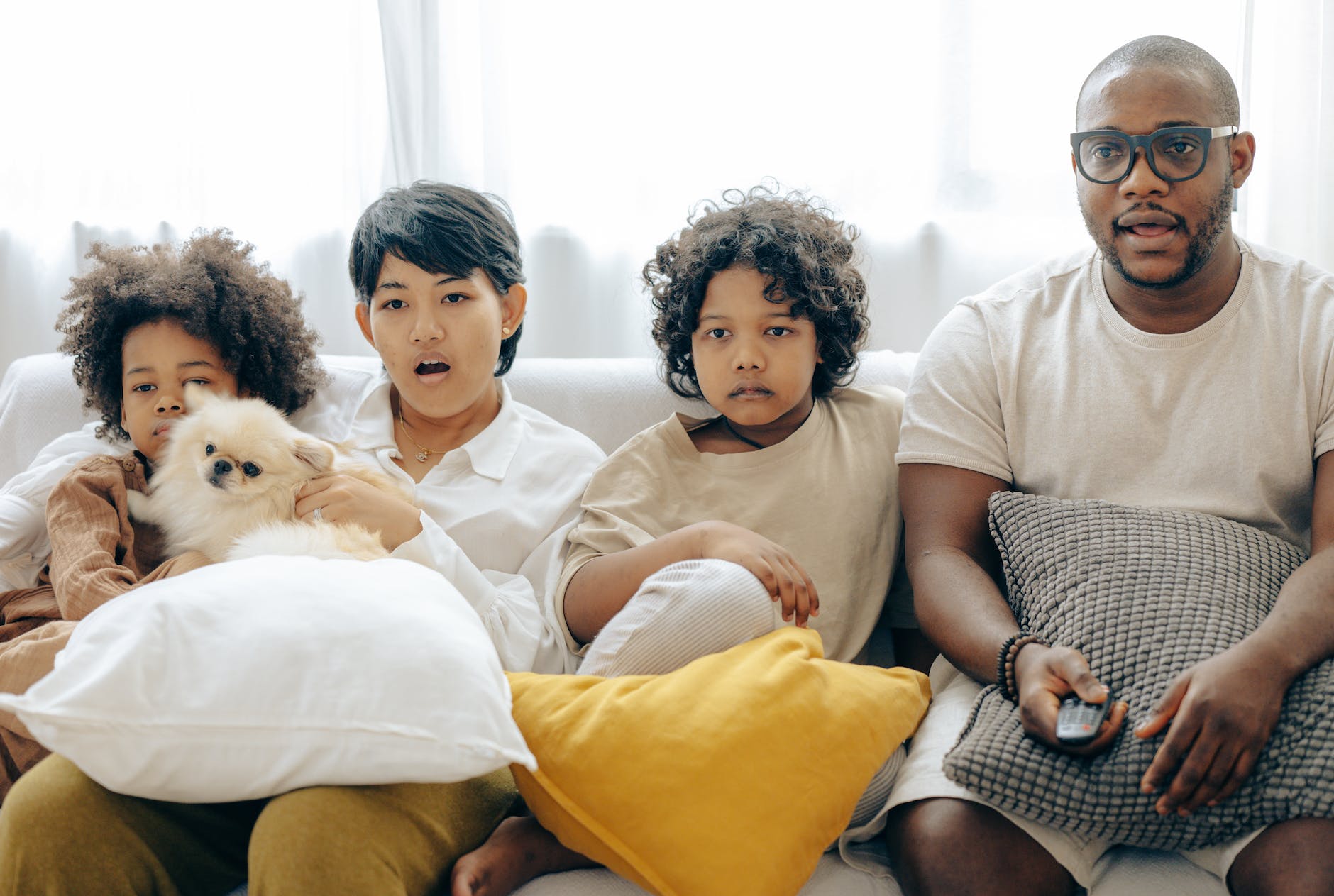 interested multiracial family watching tv on sofa together with dog
