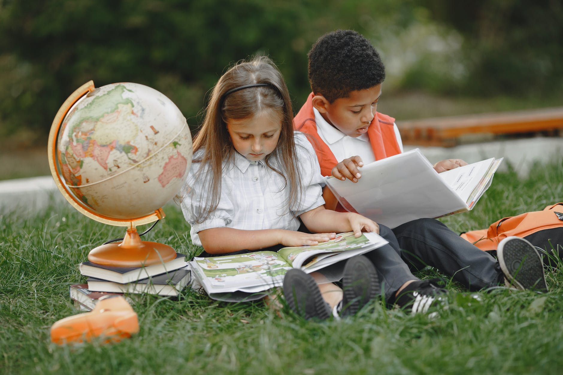 a boy and a girl sitting on grass with textbooks and a globe