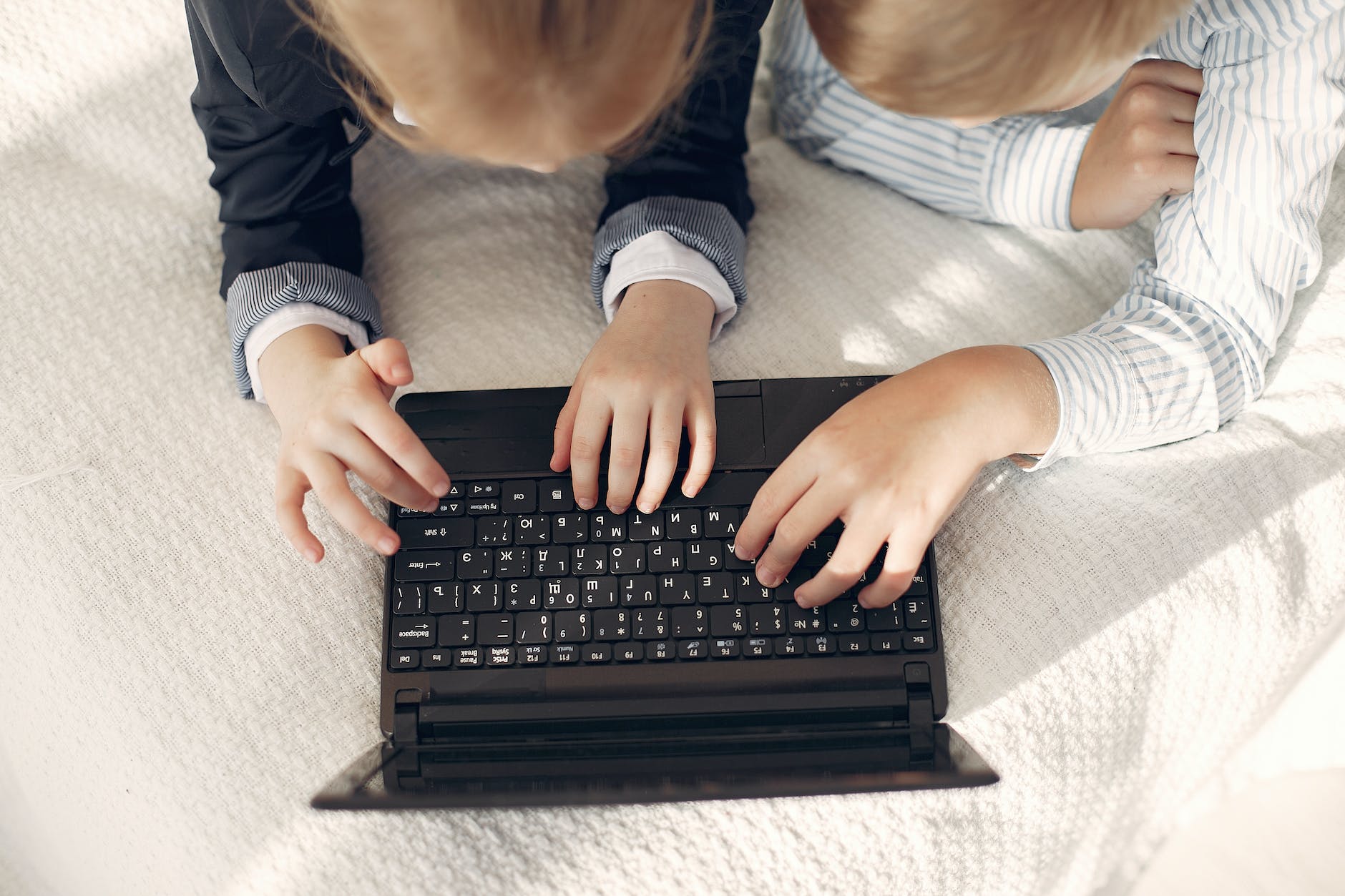 little kids using laptop together lying on bed