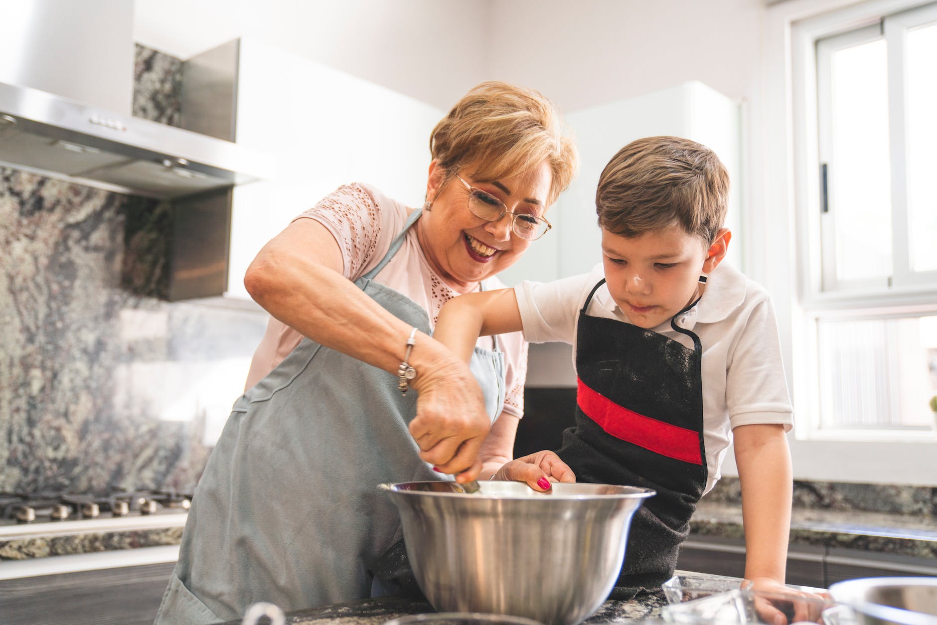 boy in white shirt and black and red apron sitting on kitchen counter